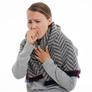 woman coughing having chills with blanket wrapped around her